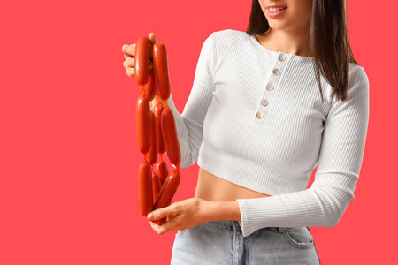 Young woman with tasty sausages on red background, closeupの写真素材