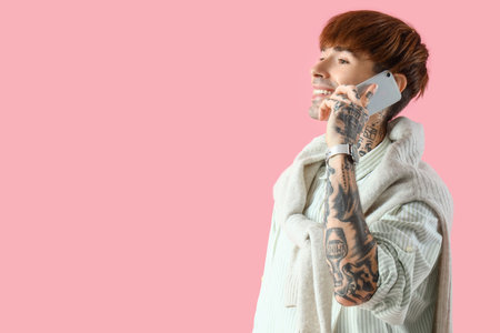 Handsome young tattooed businessman talking by mobile phone on pink backgroundの写真素材