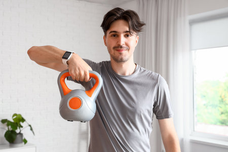 Sporty young man doing exercise with kettlebell at homeの写真素材
