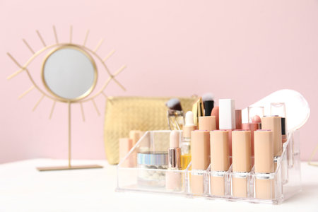 Holder with different makeup products and mirror on dressing table near pink wall in roomの写真素材