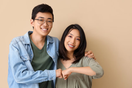 Young Asian friends bumping fists on beige backgroundの写真素材