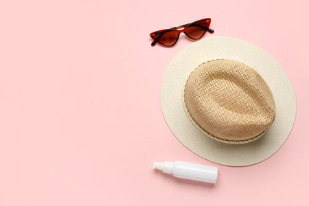 Stylish straw hat, sunglasses and bottle of sunscreen cream on color background