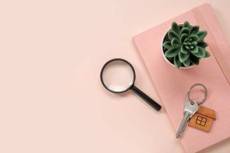Magnifier, notebook and key with trinket in house shape on pink background. Concept of buying real...