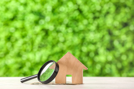 House figure with magnifier and money on white table against decorative green grass. Concept of buying real estateの写真素材