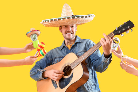 Young man playing guitar and hands with Mexican symbols on yellow backgroundの写真素材