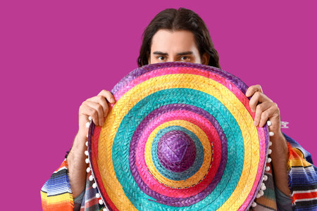 Handsome young Mexican man in sombrero on magenta background