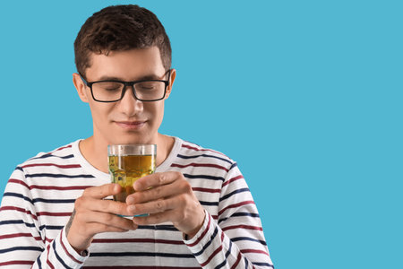 Young man with glass of juice on blue background, closeup