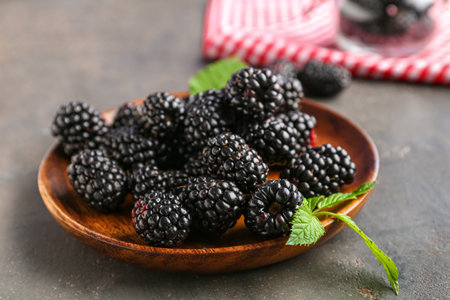 Wooden plate with fresh blackberries on gray backgroundの写真素材