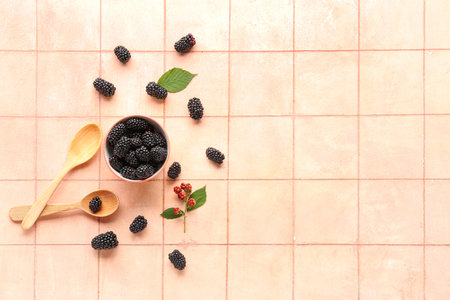 Bowl and wooden spoon with fresh blackberries on pink tile backgroundの写真素材