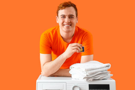 Young man with capsule laundry and towels on orange backgroundの写真素材