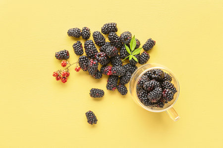 Glass cup with fresh blackberries on yellow background