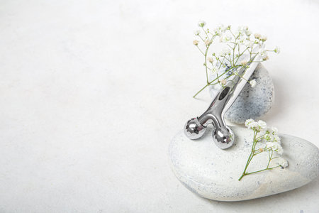 Metal face massage roller and spa stones on light backgroundの写真素材