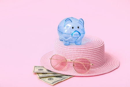 Piggy bank with beach accessories and money on pink background. Concept of savings for travelの写真素材