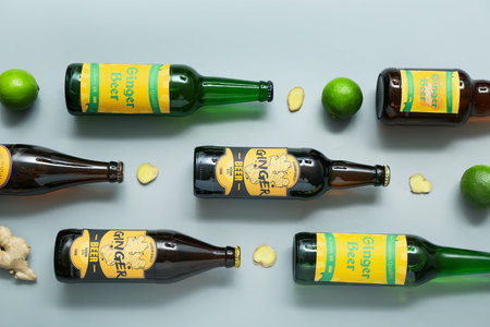 Composition with different bottles of fresh ginger beer and lime on gray background