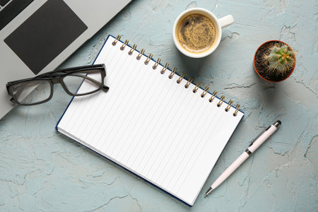 Notebook with eyeglasses and cup of tasty coffee on blue background