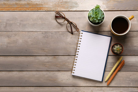 Notebook with eyeglasses and cup of tasty coffee on gray wooden background