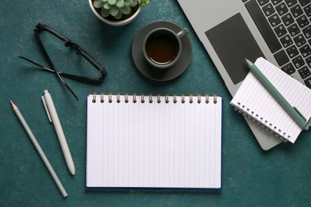 Notebooks with laptop and cup of tasty coffee on green background