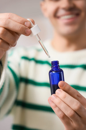 Young man with bottle of CBD oil at home, closeup