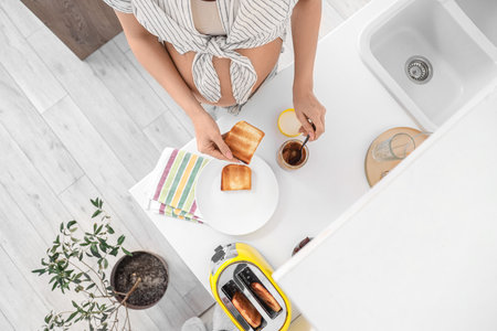 Young pregnant woman spreading peanut butter onto toast in kitchen, top viewの写真素材