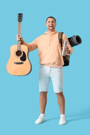 Male tourist with backpack, thermos and guitar on blue backgroundの写真素材
