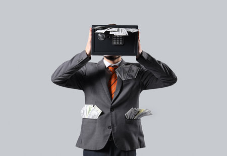 Young man with safe box and money on gray backgroundの写真素材