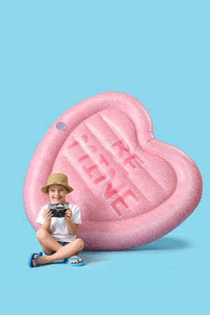Cute little boy with photo camera and heart-shaped swim mattress on blue background