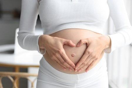 Young pregnant woman making heart gesture at home, closeup