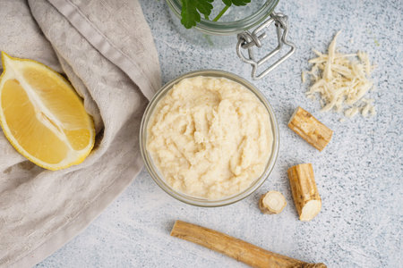 Horseradish sauce in glass bowl with lemon and horseradish roots on white backgroundの写真素材