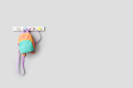 Stylish school backpack hanging on light wall