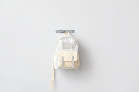 Stylish school backpack hanging on light wall