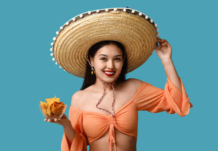 Portrait of young woman with sombrero and tortilla chips on blue background. National Tortilla Chip Day celebrationの写真素材