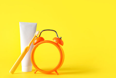 Alarm clock, toothpaste and toothbrush on yellow backgroundの写真素材