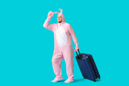 Young man in bunny costume with suitcase on blue background. Easter celebrationの写真素材