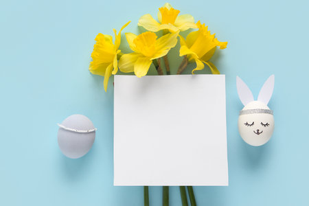 Yellow narcissus, decorated Easter eggs and empty paper sheet on blue backgroundの写真素材