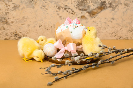 Wooden board with tasty Easter cake, egg, chicks and willow branches on brown table