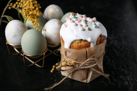 Sweet Easter cake, mimosa flowers and holder with eggs on black backgroundの写真素材