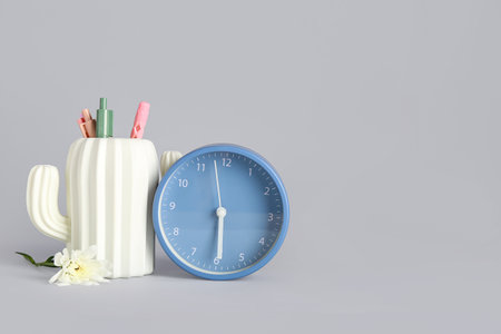 Alarm clock with chrysanthemum flower and holder in shape of cactus on gray backgroundの写真素材