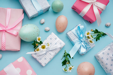 Painted Easter eggs with gift boxes and chamomile flowers on blue backgroundの写真素材