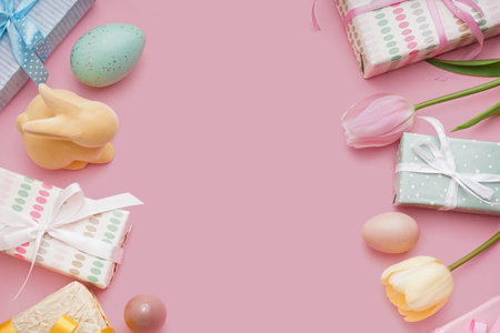 Frame made of pained Easter eggs with gift boxes, toy bunny and tulip flowers on pink backgroundの写真素材