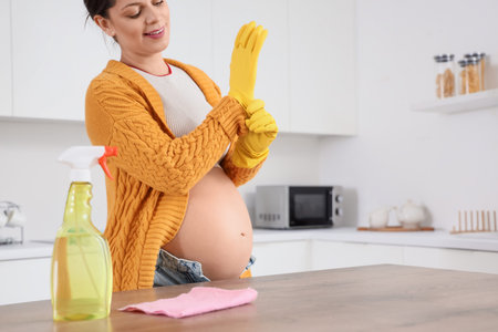 Young pregnant woman putting on rubber gloves in kitchen