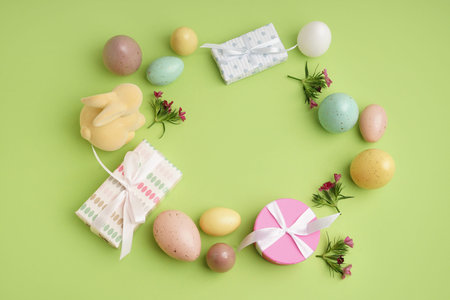 Beautiful wreath made of Easter eggs, flowers and gift box on green background