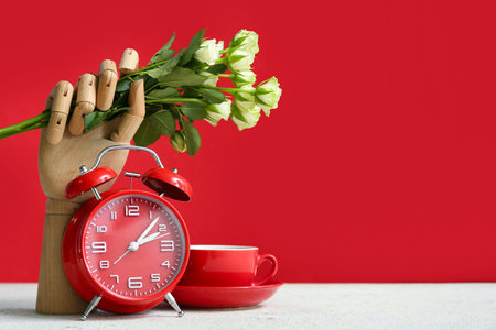 Wooden hand with rose flowers, alarm clock and cup on white tableの写真素材