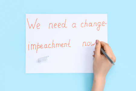 Woman writing text WE NEED A CHANGE - IMPEACHMENT NOW on picket poster against blue backgroundの写真素材