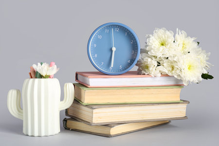 Alarm clock with books and chrysanthemum flowers on gray backgroundの写真素材