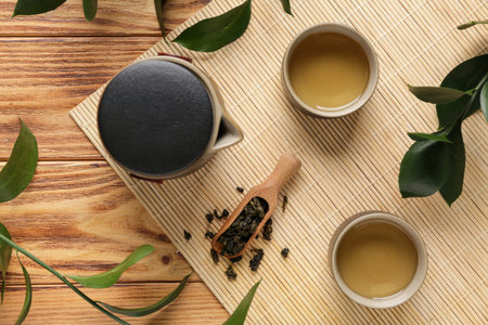 Cups of tasty tea, teapot and spoon with dry leaves on wooden background