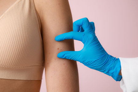 Dermatologist examining young woman with moles on pink background, closeup