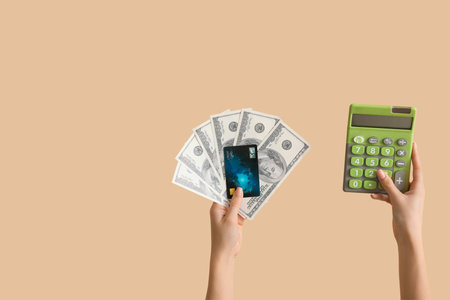 Woman with credit card, calculator and dollar banknotes on beige backgroundの写真素材