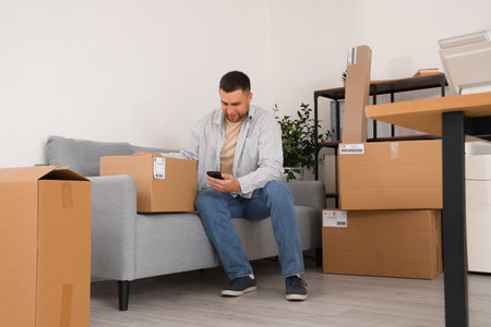 Male seller with parcel and mobile phone sitting in warehouse store