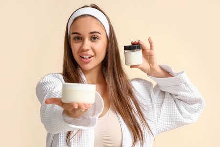Beautiful young woman with jars of coconut oil on beige backgroundの写真素材