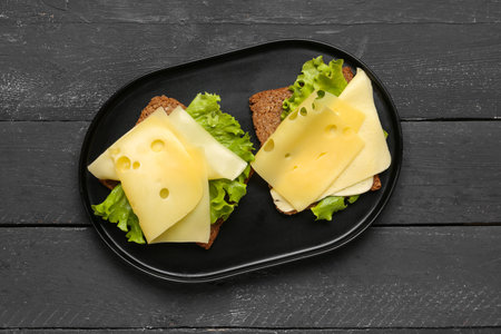 Tasty sandwiches with cheese and lettuce on dark wooden background